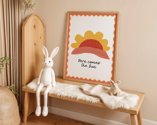 Charmantes Poster "Here Comes the Sun" von justgoodmood, mit buntem Sonnenmotiv, lächelndem Stoffhasen und gemütlicher Bank im Kinderzimmer.