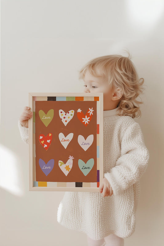 Ein Kind hält ein fröhliches Poster mit Herzen und Blumenmustern für das Kinderzimmer von JUSTGOODMOOD. Warmes Design für eine liebevolle Wanddekoration.