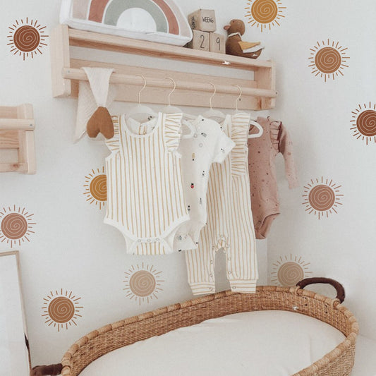 Gestalte das Kinderzimmer mit den Wandaufklebern von justgoodmood im Boho Stil. Nachwuchsbekleidung hängt an einem Holzregal vor fröhlichen Wandtattoos.