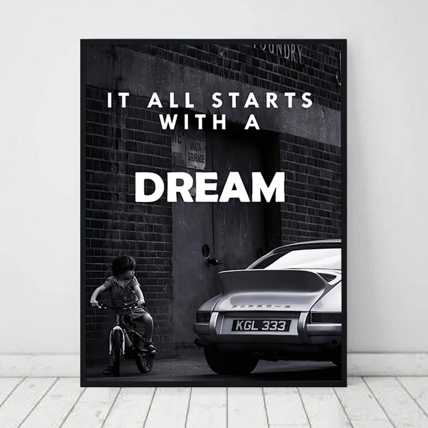 Inspirierendes Poster von justgoodmood mit dem Titel "Schwarz Weiß Luxus Geschäfte und Fahrzeuge als Deko Print ohne Rahmen". Es zeigt ein Kind auf einem Fahrrad neben einem eleganten, klassischen Auto, das den Satz "It all starts with a DREAM" in einer stilvollen Schrift betont.