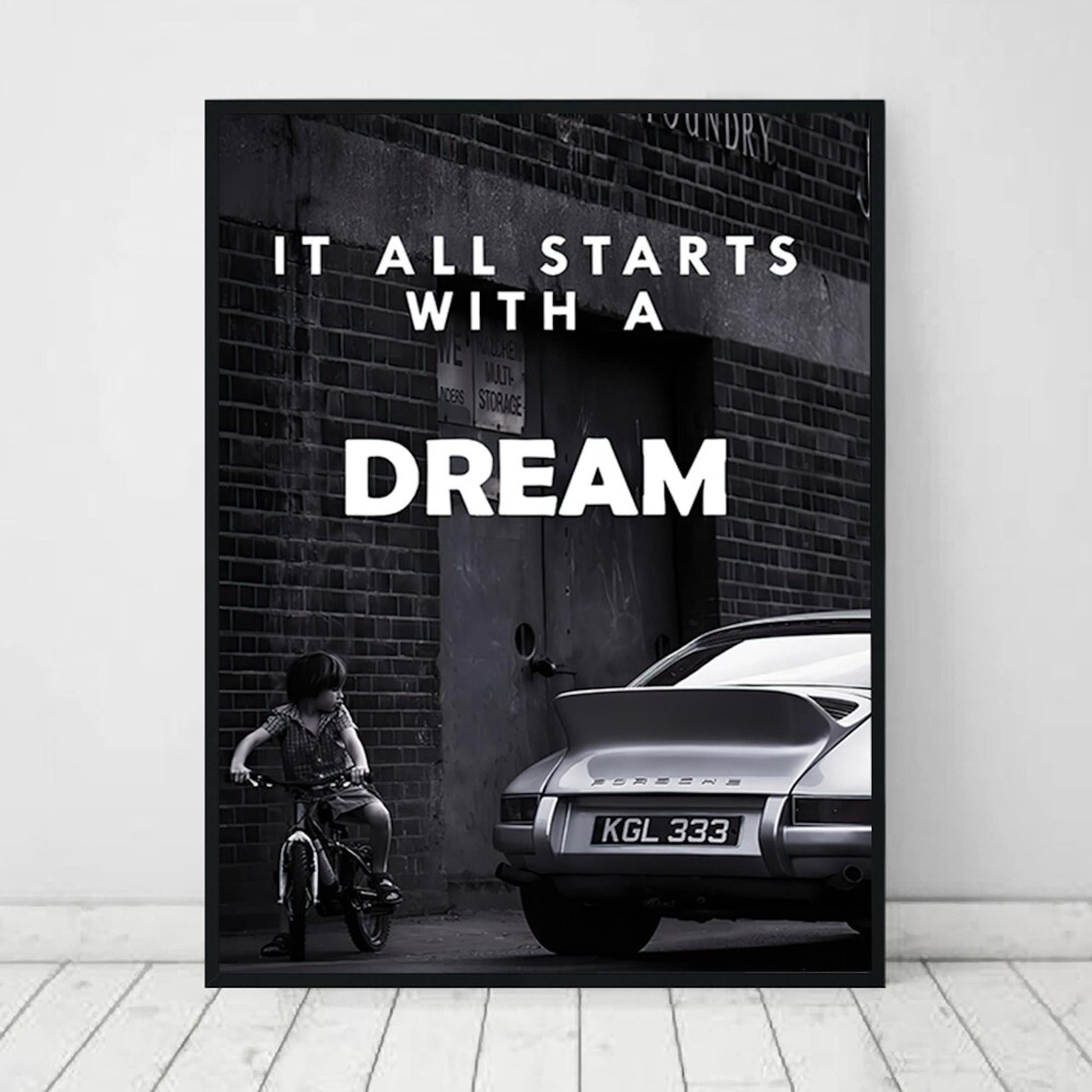 Inspirierendes Poster von justgoodmood mit dem Titel "Schwarz Weiß Luxus Geschäfte und Fahrzeuge als Deko Print ohne Rahmen". Es zeigt ein Kind auf einem Fahrrad neben einem eleganten, klassischen Auto, das den Satz "It all starts with a DREAM" in einer stilvollen Schrift betont.