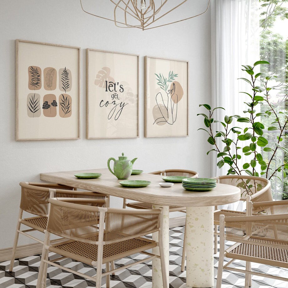 Essbereich mit dem charmanten Poster 'Let's Go Cozy' von justgoodmood, perfekt platziert über einem modernen Tisch, voller Pflanzen und natürlicher Lichtquellen.