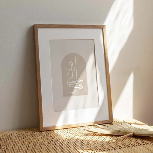 Poster mit islamischer Kalligraphie von justgoodmood, gerahmt in einem Holzrahmen und dekorativ auf einem Rattan-Tisch platziert.