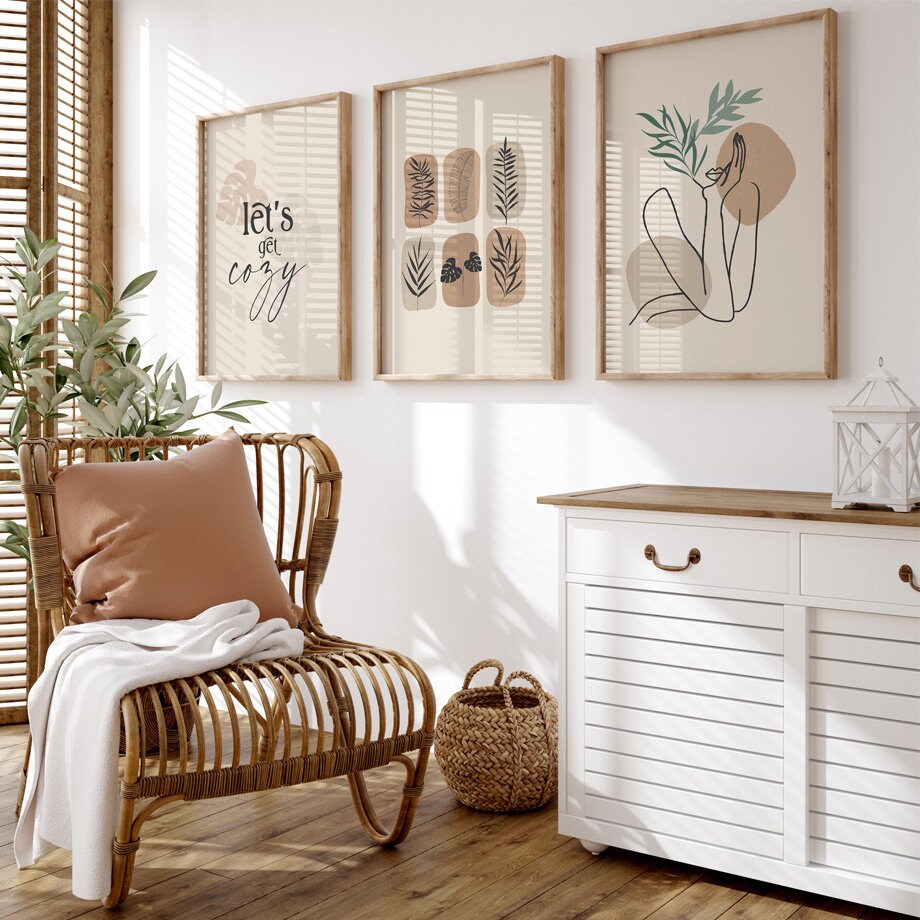 Stylische Wandbilder 'Let's Go Cozy' von justgoodmood, vorgestellt in einem sonnigen Raum mit Korbstuhl und Pflanzen, die ein warmes Ambiente schaffen.
