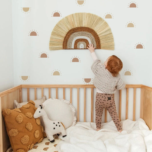 Ein fröhliches Kind im Babyzimmer mit einem Boho Stil Wandaufkleber Set von justgoodmood. Der warme, künstlerische Hintergrund mit Sonnenmotiven lässt das Zimmer lebendig wirken, während das Kind den kreativen Wandaufkleber bewundert. Ideal für eine zauberhafte Wandgestaltung im Kinderzimmer!