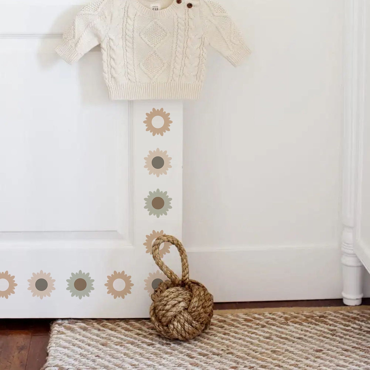 Süße Blumen Wandaufkleber von justgoodmood, die das Kinderzimmer in eine fantasievolle Oase verwandeln. Die Wandtattoos sind am Türrahmen mit einem weißen Pullover und einem dekorativen Wollknäuel zu sehen.