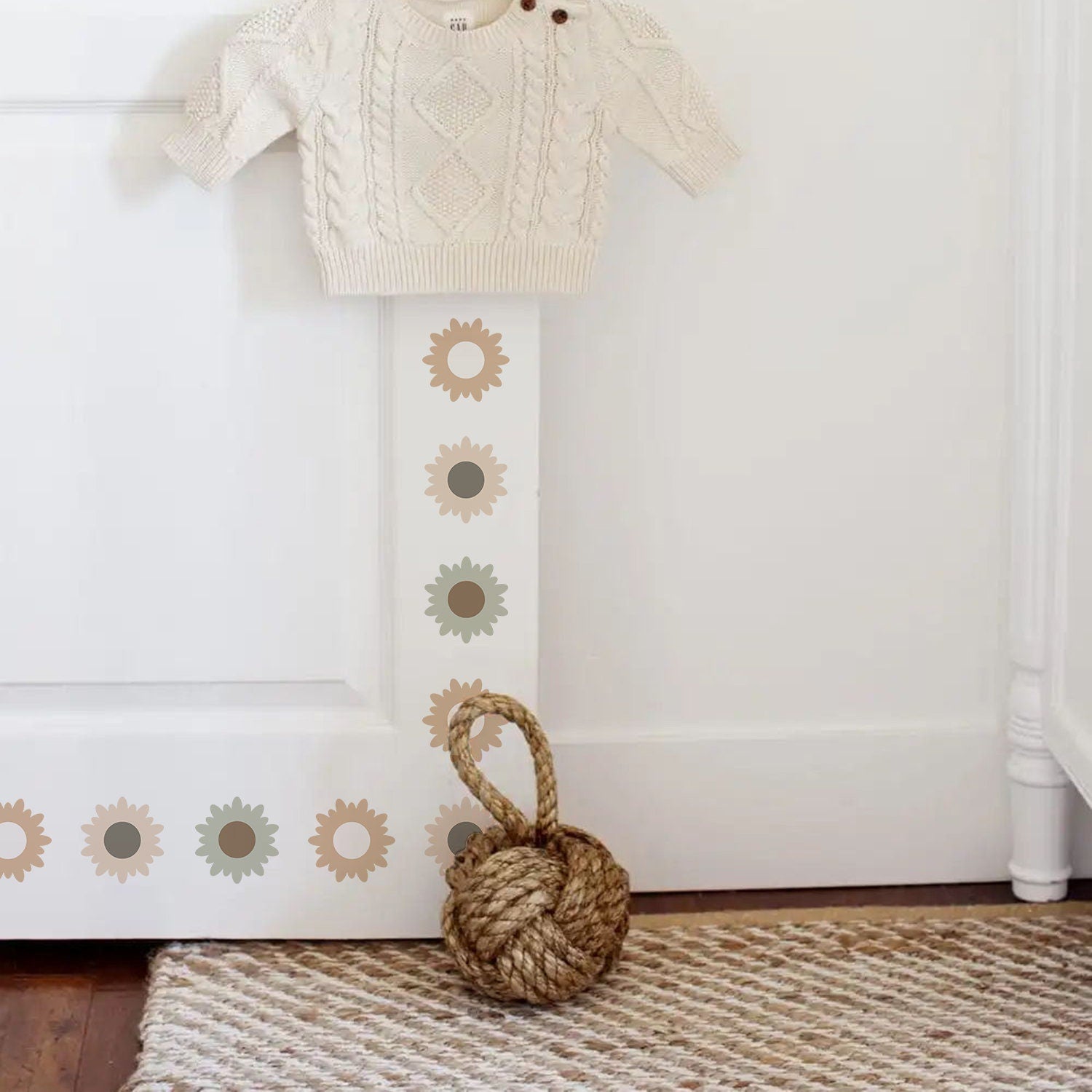 Süße Blumen Wandaufkleber von justgoodmood, die das Kinderzimmer in eine fantasievolle Oase verwandeln. Die Wandtattoos sind am Türrahmen mit einem weißen Pullover und einem dekorativen Wollknäuel zu sehen.