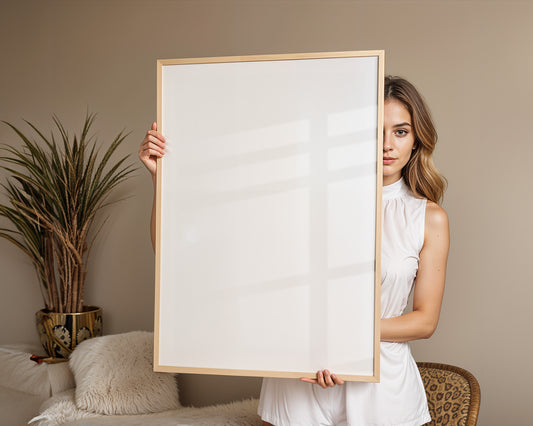 Eine Frau hält einen leeren Rahmen vor sich und zeigt, wie einfach es ist, ein personalisierbares Poster von JUSTGOODMOOD zu gestalten.