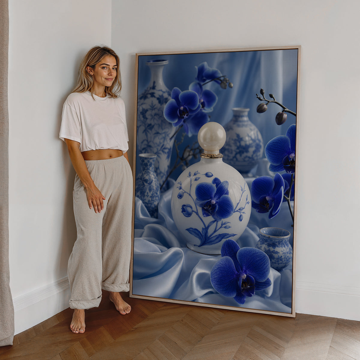 Motiv mit einem weiß-blauen Parfumflakon zwischen blauen Orchideen und Porzellanvasen, als großes gerahmtes Wandbild neben einer Frau.