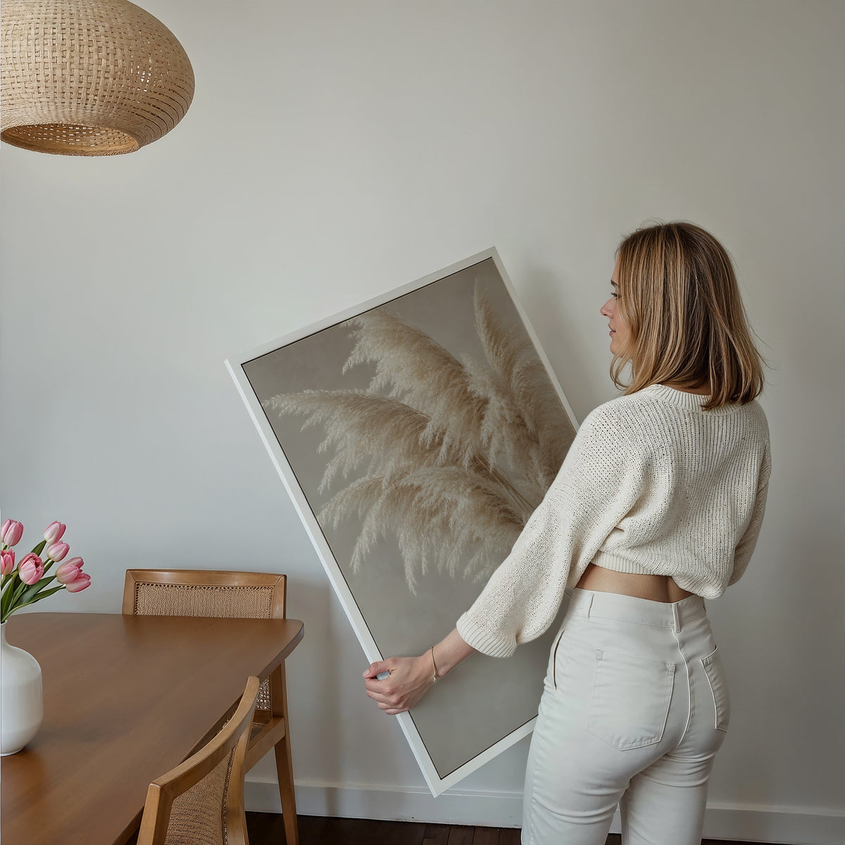 Motiv mit cremeweißen Pampasgräsern an feinen Stielen vor greigefarbenem Hintergrund, über einem Bett im hellen Schlafzimmer.