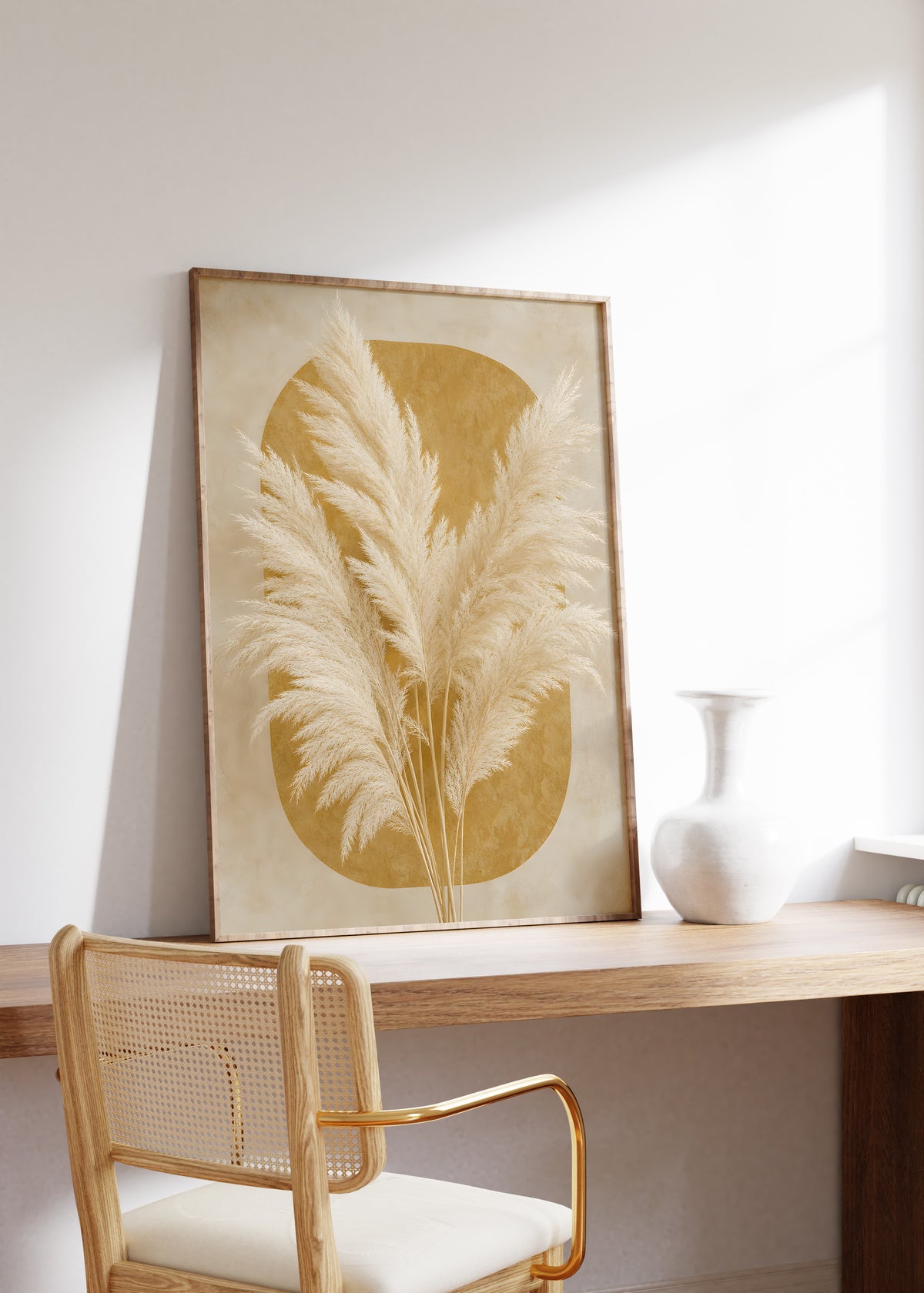 Gerahmtes Poster mit cremeweißen Pampaswedeln vor einer ockerfarbenen abgerundeten Form, auf einem Holztisch neben einer weißen Vase.