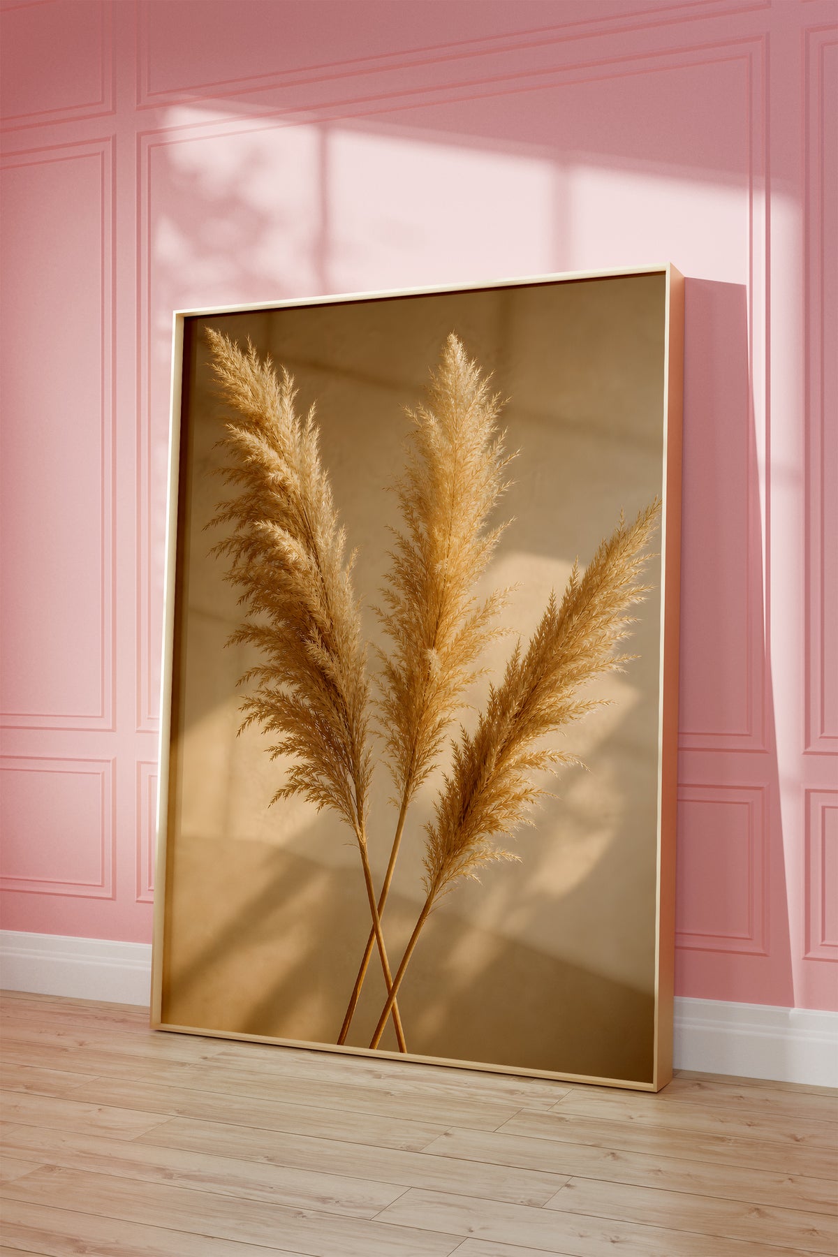Motiv mit drei goldenen Pampaswedeln mit langen Schatten auf warmbeigem Hintergrund, als gerahmtes Poster vor einer rosafarbenen Wand.