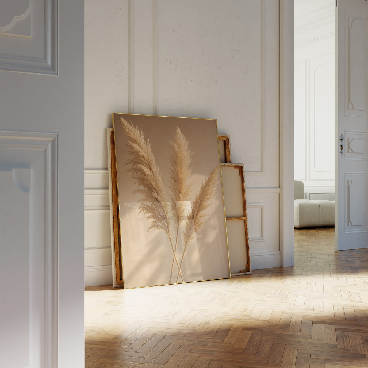 Motiv mit drei goldenen Pampaswedeln mit langen Schatten auf warmbeigem Hintergrund, als an die Wand gelehntes Poster neben leeren Rahmen.