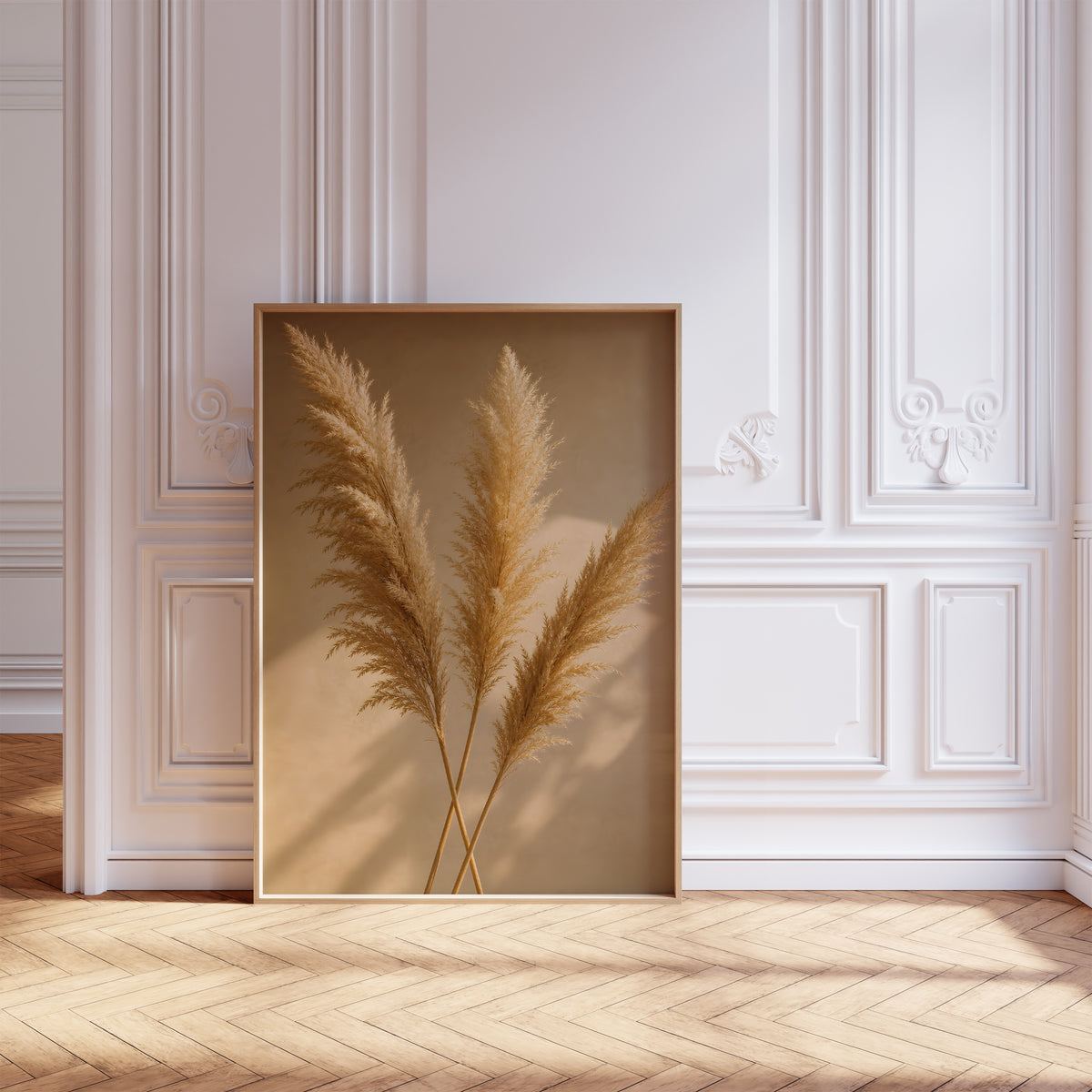 Gerahmtes Poster mit drei goldenen Pampaswedeln mit langen Schatten auf warmbeigem Hintergrund, vor einer weißen Wand mit Zierleisten.