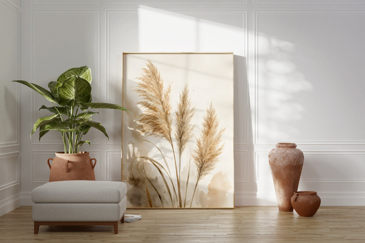 Motiv mit drei beigen Pampaswedeln mit zarten Aquarellflächen, als gerahmtes Poster neben Sessel und Zimmerpflanze.
