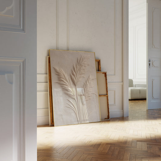 Motiv mit drei hellen Pampaswedeln in Reliefoptik auf einer beigegrauen strukturierten Fläche, als an die Wand gelehntes Poster neben leeren Rahmen.
