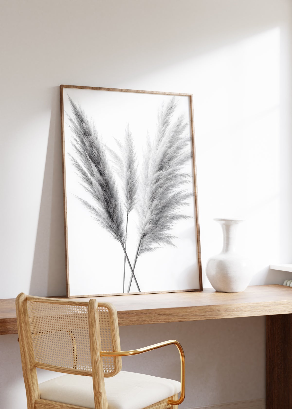 Gerahmtes Poster mit drei gekreuzten Pampaswedeln in Schwarz-Weiß vor weißem Hintergrund, auf einem Holztisch neben einer weißen Vase.