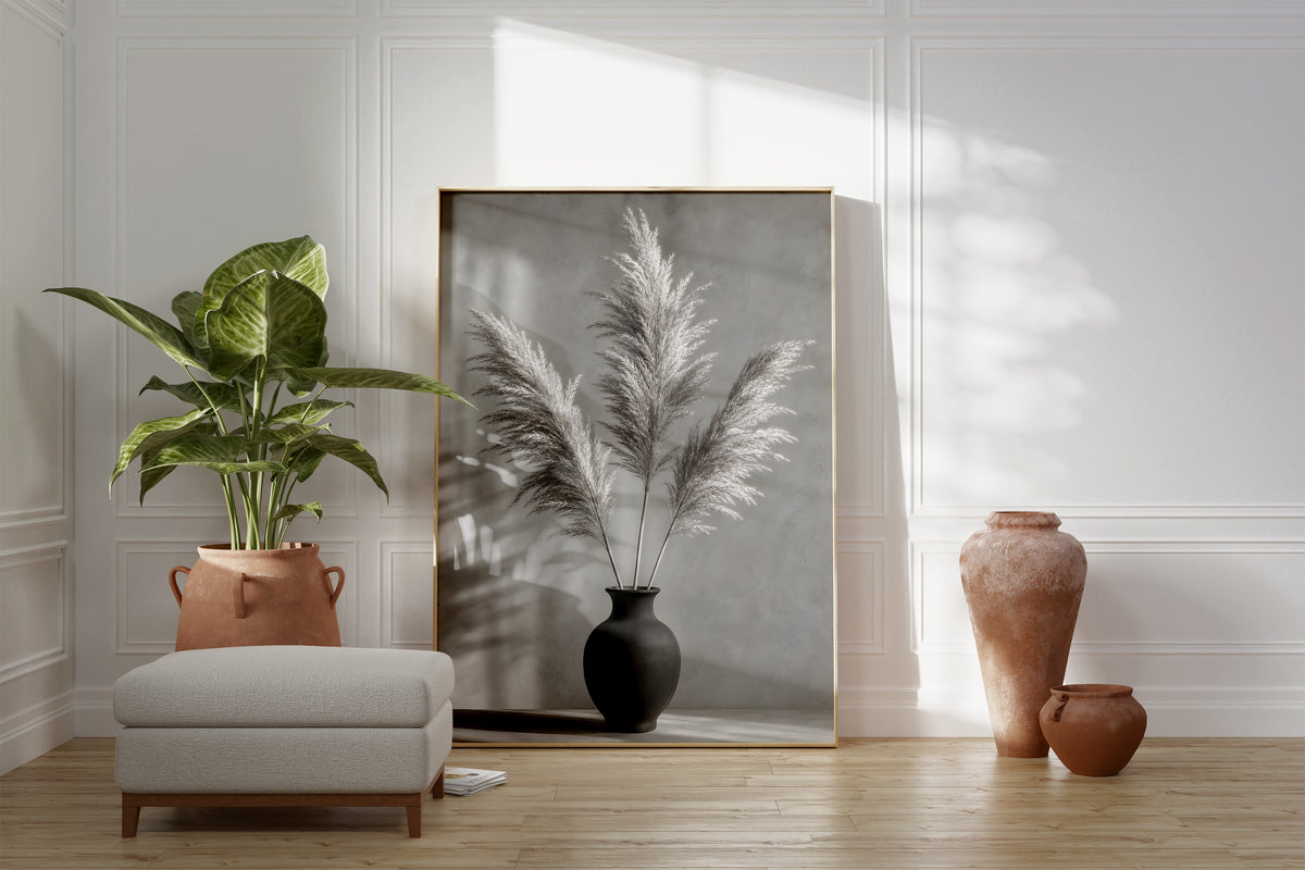Motiv mit drei Pampaswedeln in einer schwarzen Vase vor einer grauen Wand mit Schatten, als gerahmtes Poster neben Sessel und Zimmerpflanze.
