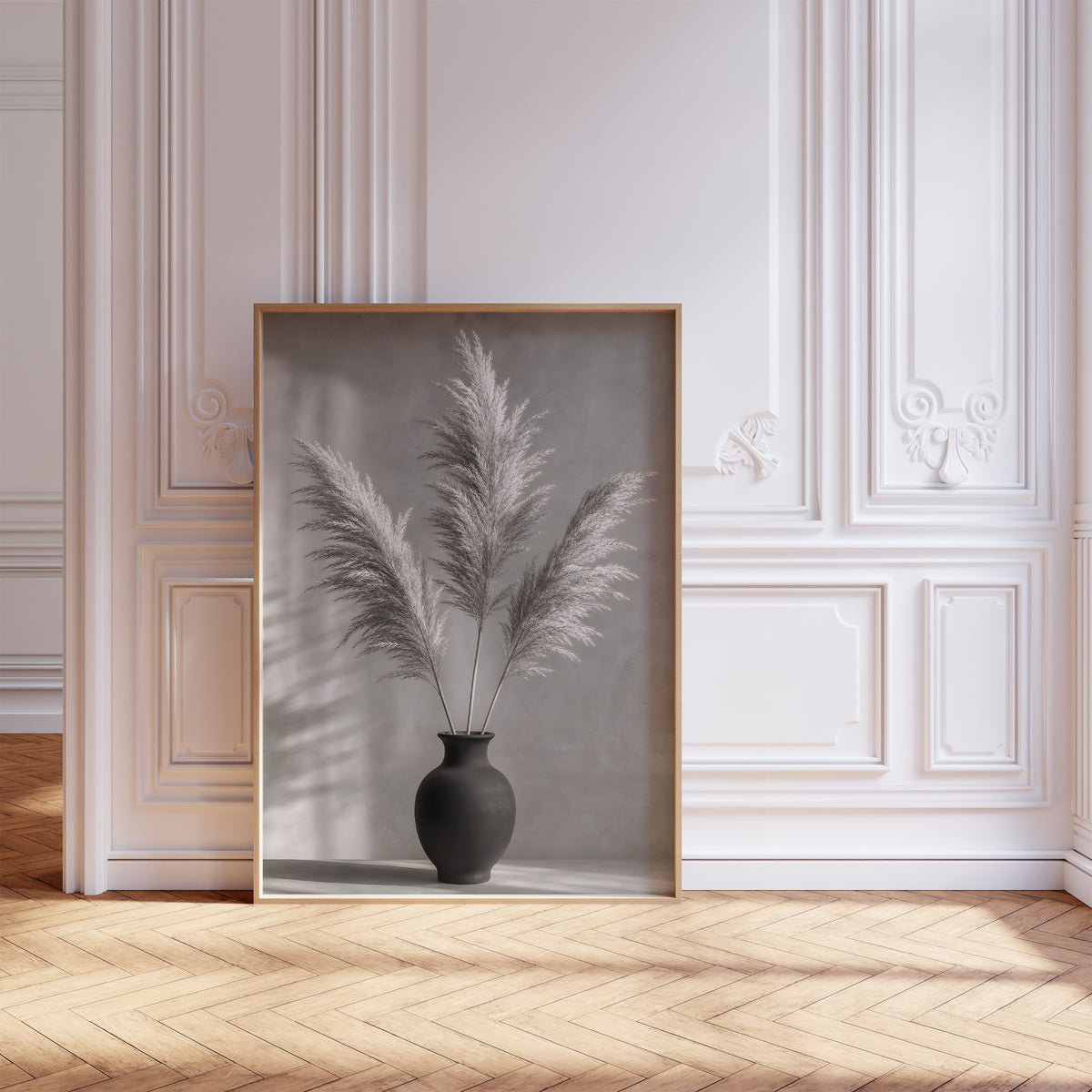 Gerahmtes Poster mit drei Pampaswedeln in einer schwarzen Vase vor einer grauen Wand mit Schatten, vor einer weißen Wand mit Zierleisten.