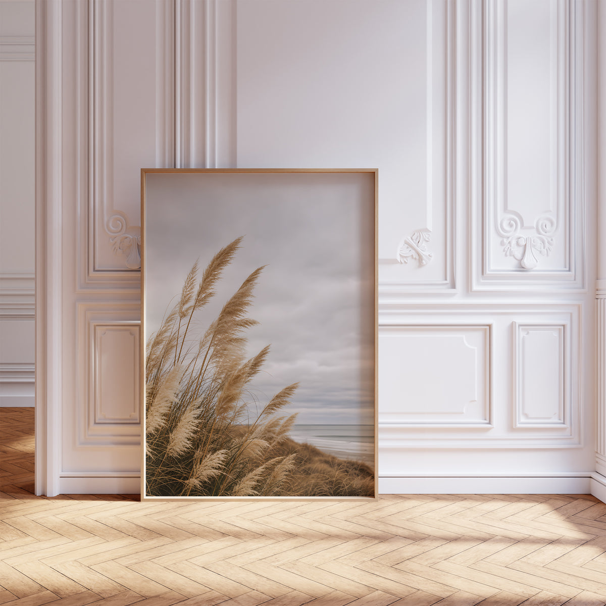 Gerahmtes Poster mit goldbraunem Dünengras am Strand unter grauen Wolken, vor einer weißen Wand mit Zierleisten.