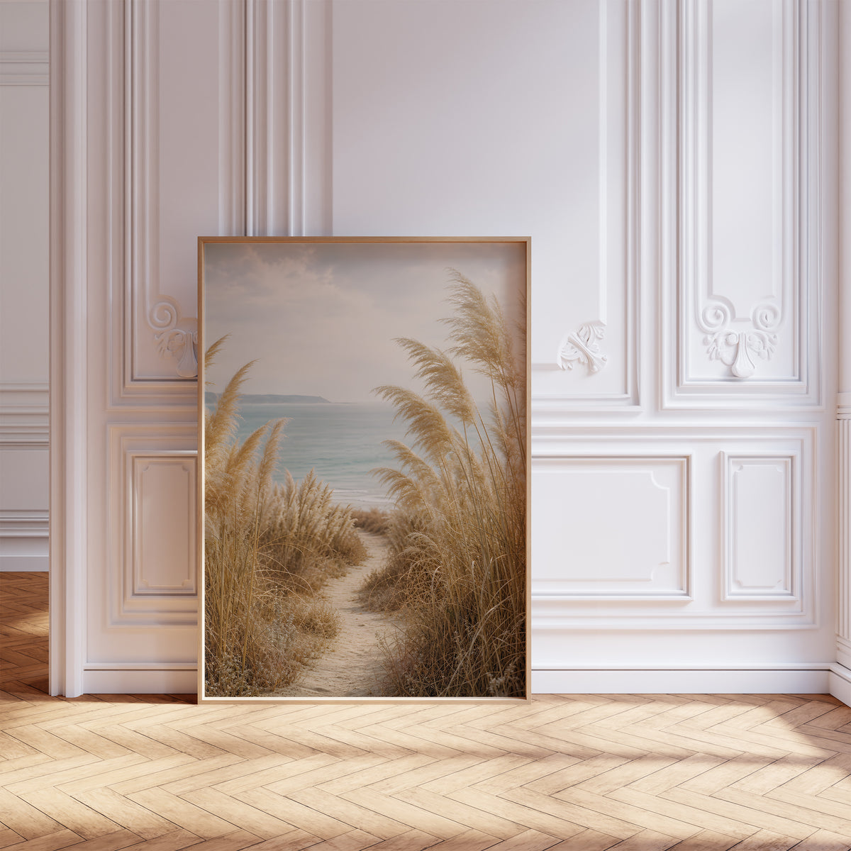 Gerahmtes Poster mit einem schmalen Sandpfad zwischen Pampasgräsern zum blauen Meer, vor einer weißen Wand mit Zierleisten.