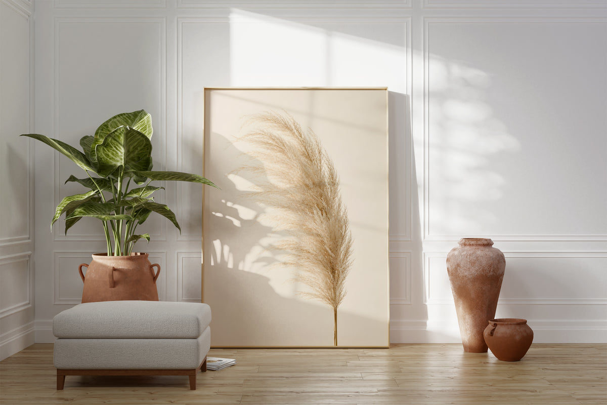 Motiv mit einem einzelnen flauschigen Pampaswedel in Cremebeige vor hellem Hintergrund, als gerahmtes Poster neben Sessel und Zimmerpflanze.