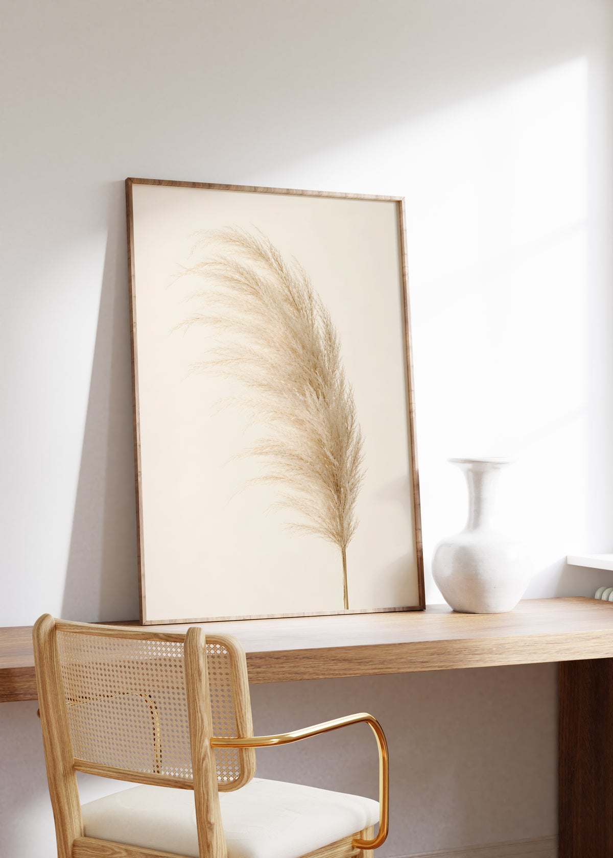 Gerahmtes Poster mit einem einzelnen flauschigen Pampaswedel in Cremebeige vor hellem Hintergrund, auf einem Holztisch neben einer weißen Vase.