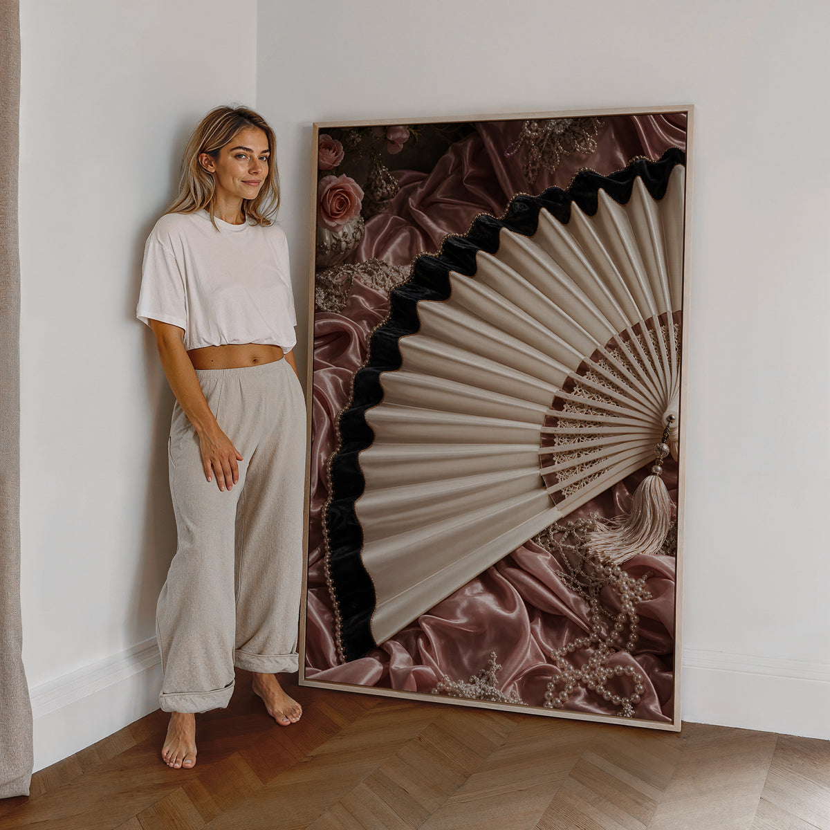Motiv mit einem cremefarbenen Fächer mit schwarzem Saum auf roséfarbenem Satin, als großes gerahmtes Wandbild neben einer Frau.