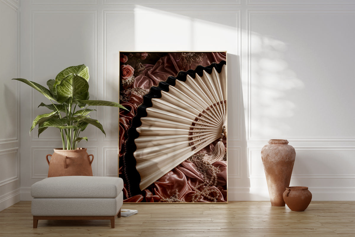 Motiv mit einem cremefarbenen Fächer mit schwarzem Saum auf roséfarbenem Satin, als gerahmtes Poster neben Sessel und Zimmerpflanze.