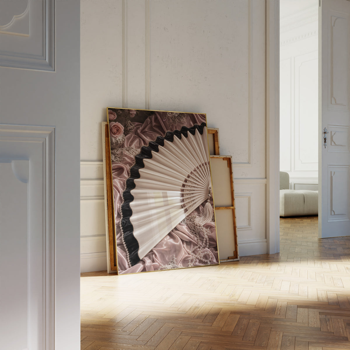 Motiv mit einem cremefarbenen Fächer mit schwarzem Saum auf roséfarbenem Satin, als an die Wand gelehntes Poster neben leeren Rahmen.