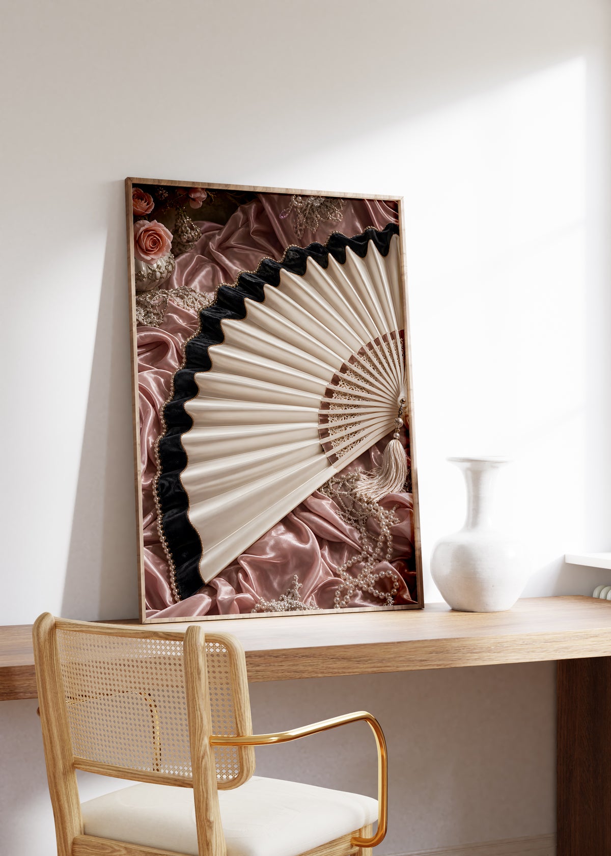 Gerahmtes Poster mit einem cremefarbenen Fächer mit schwarzem Saum auf roséfarbenem Satin, auf einem Holztisch neben einer weißen Vase.