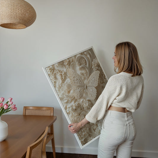 Motiv mit filigranem Schmetterling zwischen cremefarbenen Blüten und geschwungenen Reliefornamenten, als gerahmtes Poster in den Händen einer Frau.