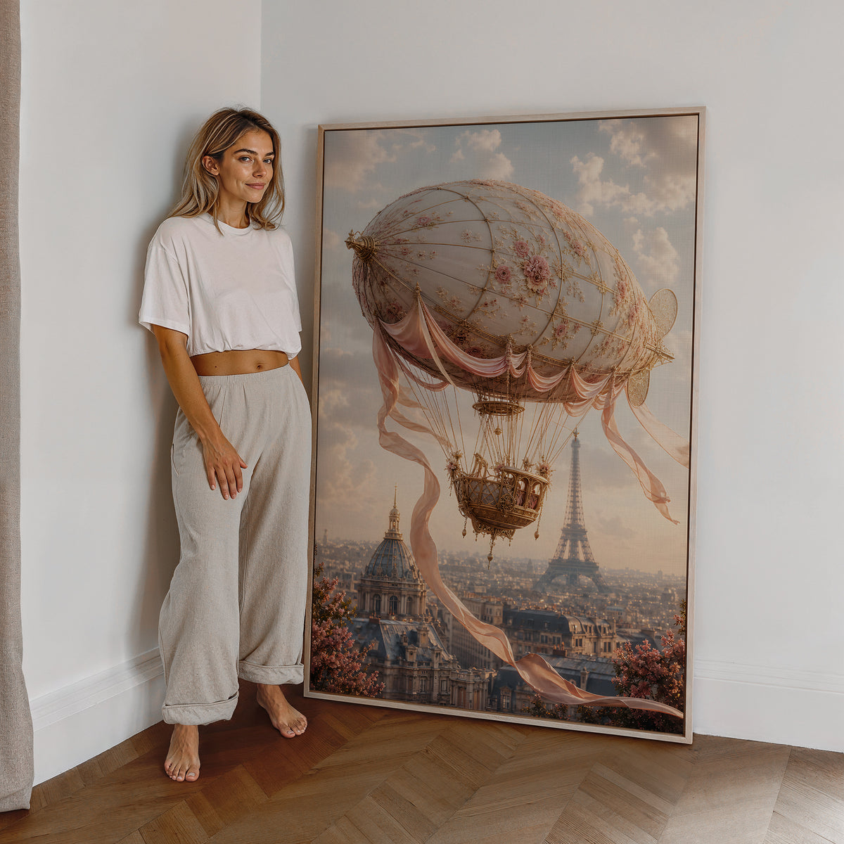 Motiv mit einem cremefarbenen Luftschiff mit Rosenmuster und Satinbändern über Paris, als großes gerahmtes Wandbild neben einer Frau.