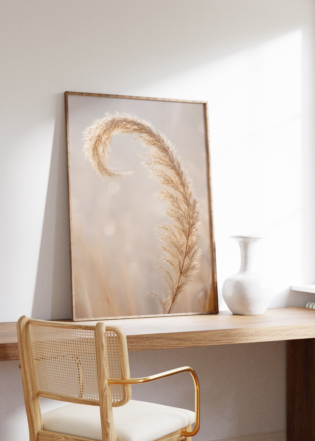 Gerahmtes Poster mit einer nach innen gebogenen beigefarbenen Pampasspitze vor weichem Hintergrund, auf einem Holztisch neben einer weißen Vase.