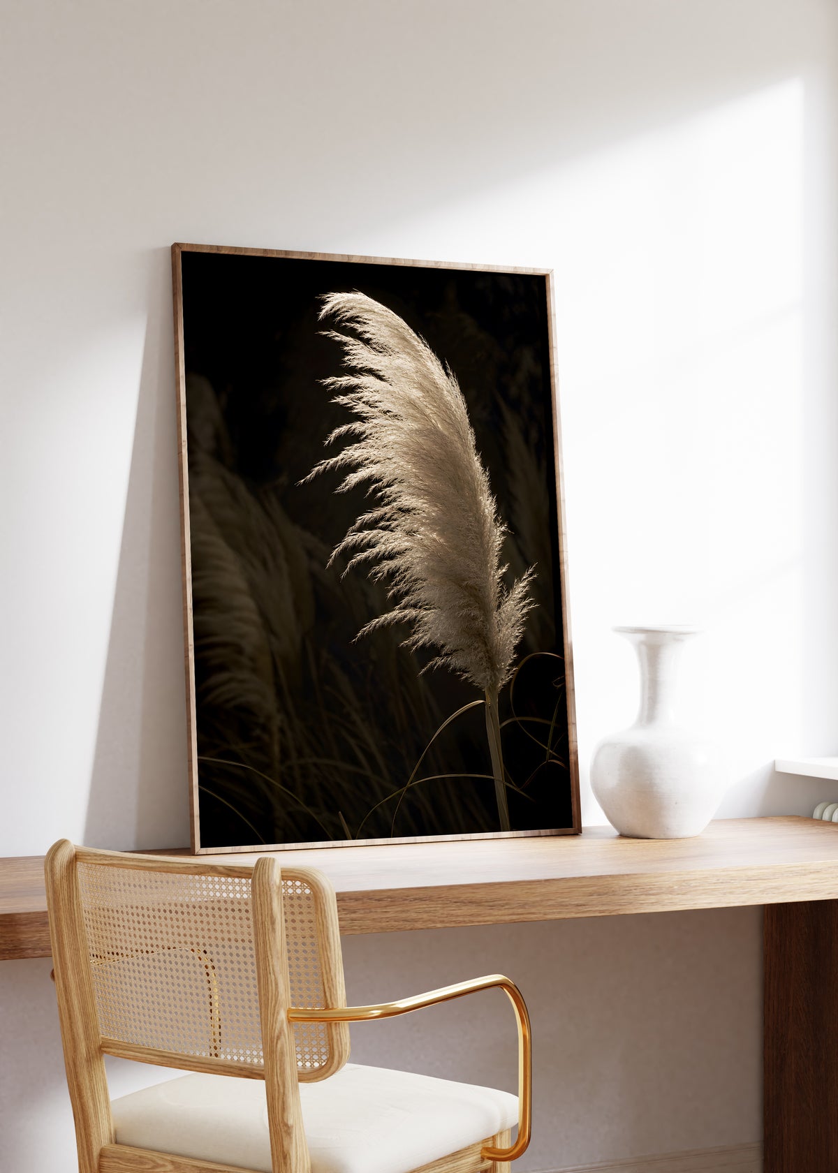 Gerahmtes Poster mit einem goldbeigen Pampaswedel vor dunklen Gräsern, auf einem Holztisch neben einer weißen Vase.