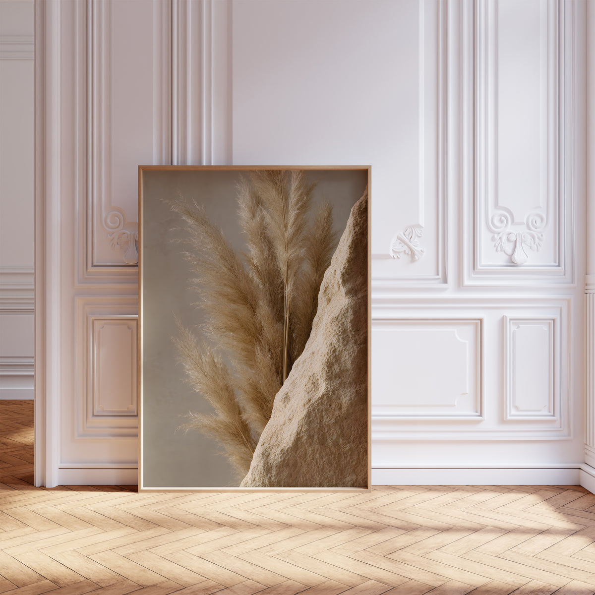 Gerahmtes Poster mit goldbraunen Pampaswedeln neben einer rauen sandfarbenen Steinfläche, vor einer weißen Wand mit Zierleisten.