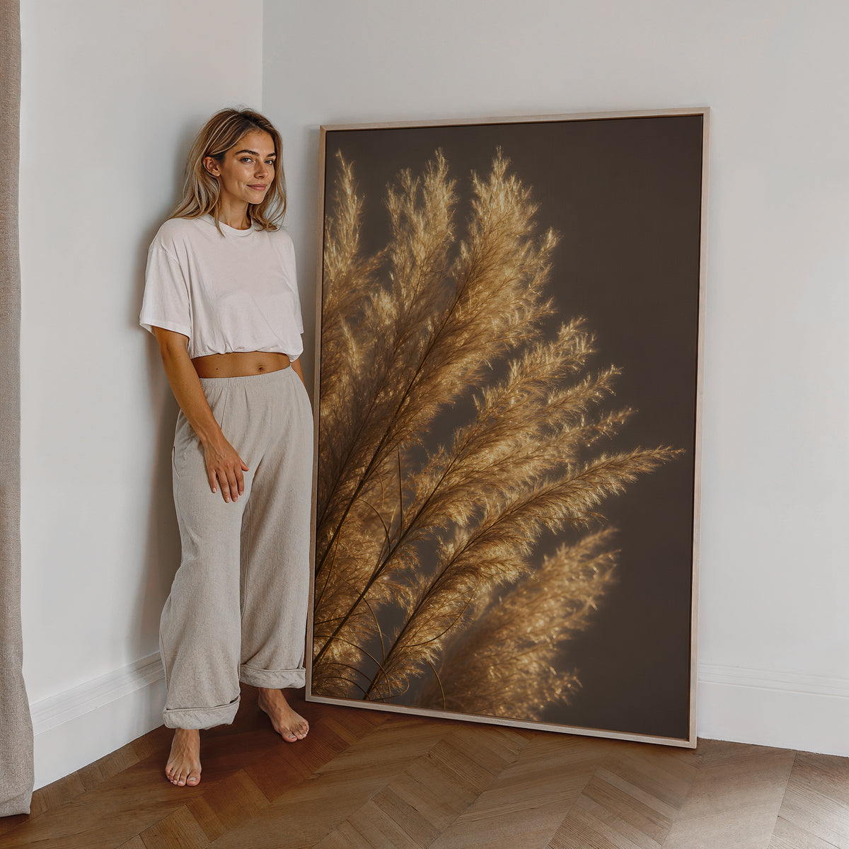 Motiv mit golden beleuchteten feinen Pampasfasern vor dunklem Hintergrund, als großes gerahmtes Wandbild neben einer Frau.