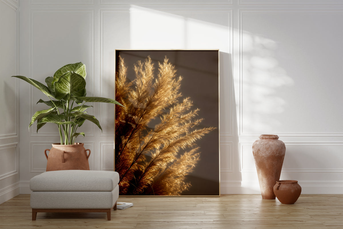 Motiv mit golden beleuchteten feinen Pampasfasern vor dunklem Hintergrund, als gerahmtes Poster neben Sessel und Zimmerpflanze.