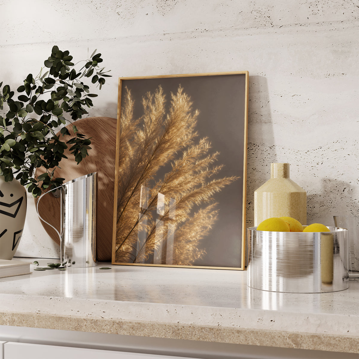 Gerahmtes Poster mit golden beleuchteten feinen Pampasfasern vor dunklem Hintergrund, auf einer Küchenarbeitsplatte neben Pflanzen und Zitronen.