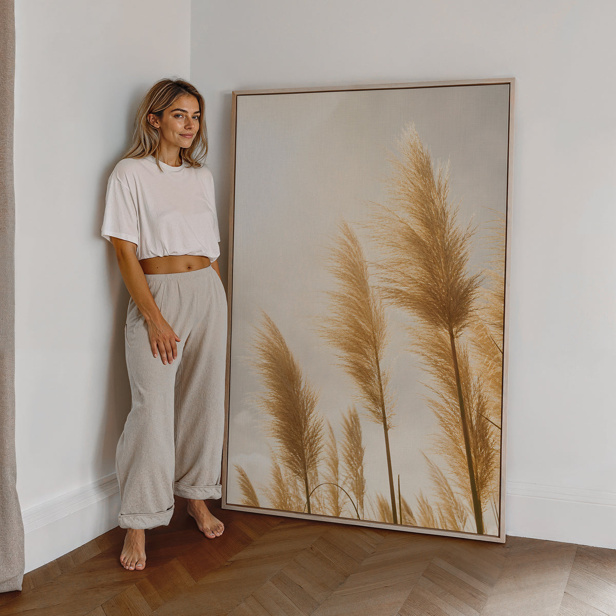 Motiv mit goldenen Pampasgräsern im hellen Gegenlicht, als großes gerahmtes Wandbild neben einer Frau.