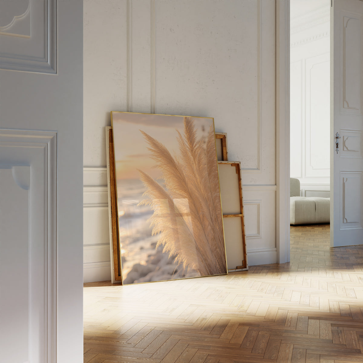 Motiv mit goldenen Pampaswedeln in Nahaufnahme am Strand im warmen Abendlicht, als an die Wand gelehntes Poster neben leeren Rahmen.