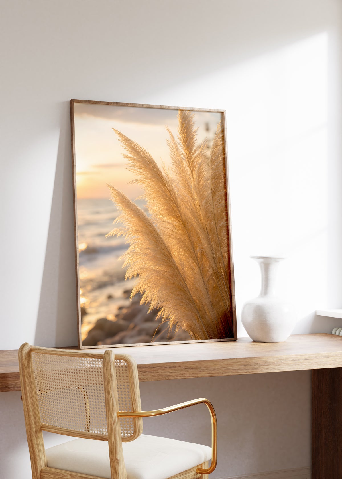 Gerahmtes Poster mit goldenen Pampaswedeln in Nahaufnahme am Strand im warmen Abendlicht, auf einem Holztisch neben einer weißen Vase.