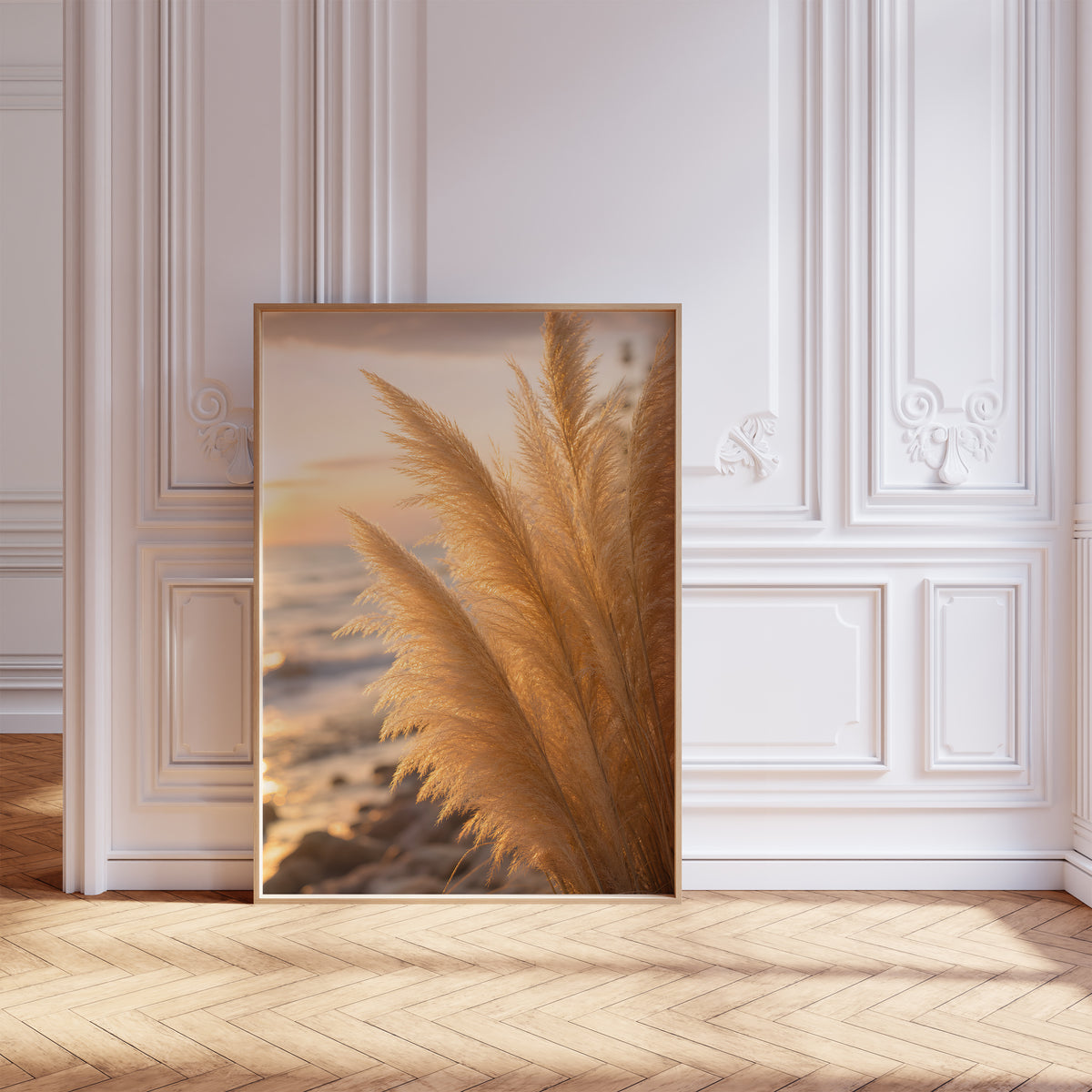Gerahmtes Poster mit goldenen Pampaswedeln in Nahaufnahme am Strand im warmen Abendlicht, vor einer weißen Wand mit Zierleisten.