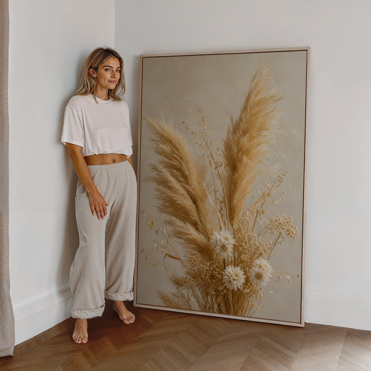 Motiv mit einem goldenen Strauß aus Pampasgras und kleinen hellen Trockenblumen, als großes gerahmtes Wandbild neben einer Frau.
