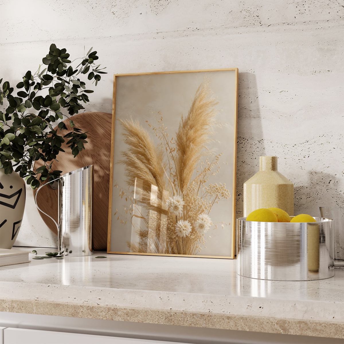 Gerahmtes Poster mit einem goldenen Strauß aus Pampasgras und kleinen hellen Trockenblumen, auf einer Küchenarbeitsplatte neben Pflanzen und Zitronen.