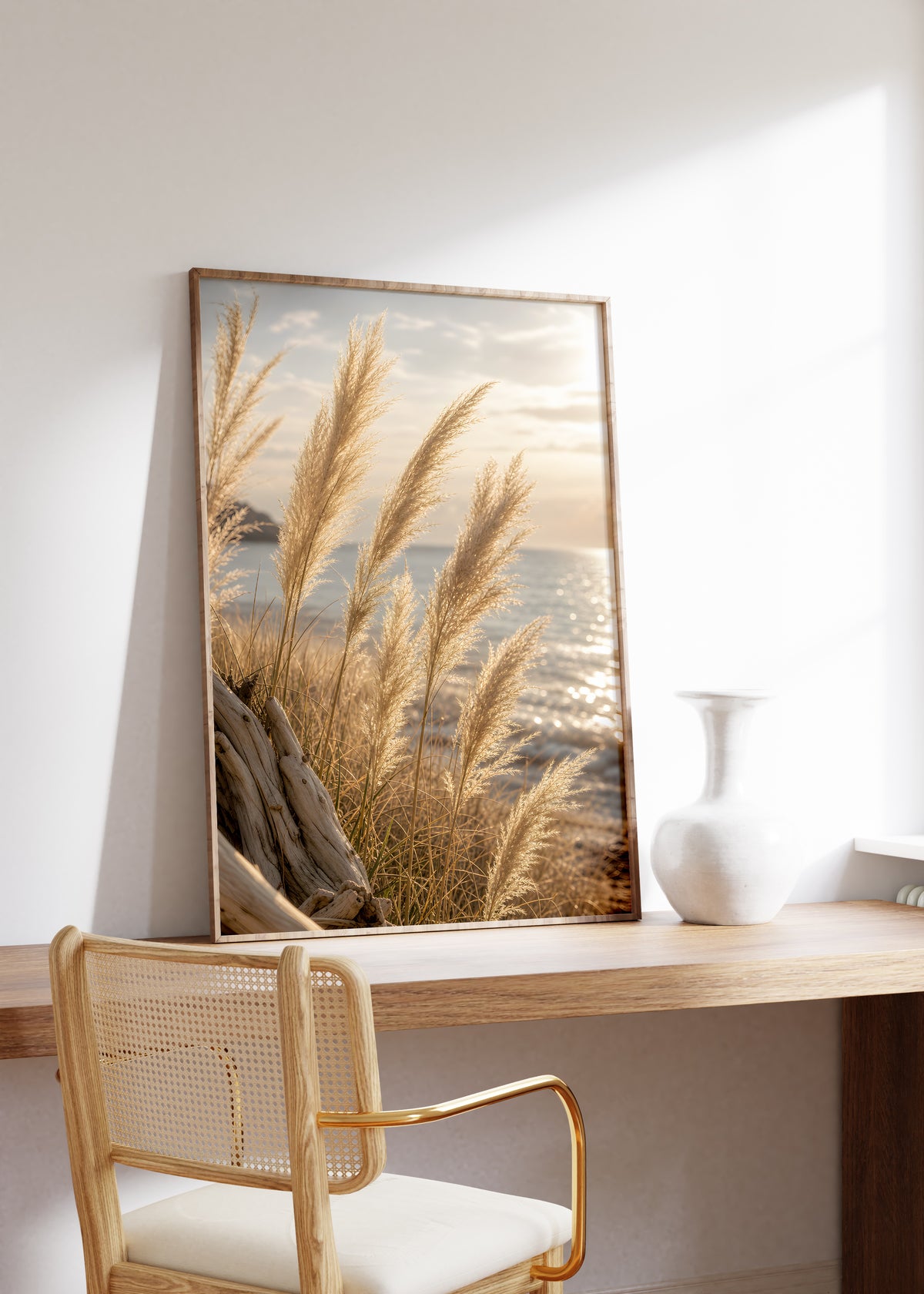 Gerahmtes Poster mit goldenen Pampasgräsern vor glitzerndem Meer im Abendlicht, auf einem Holztisch neben einer weißen Vase.