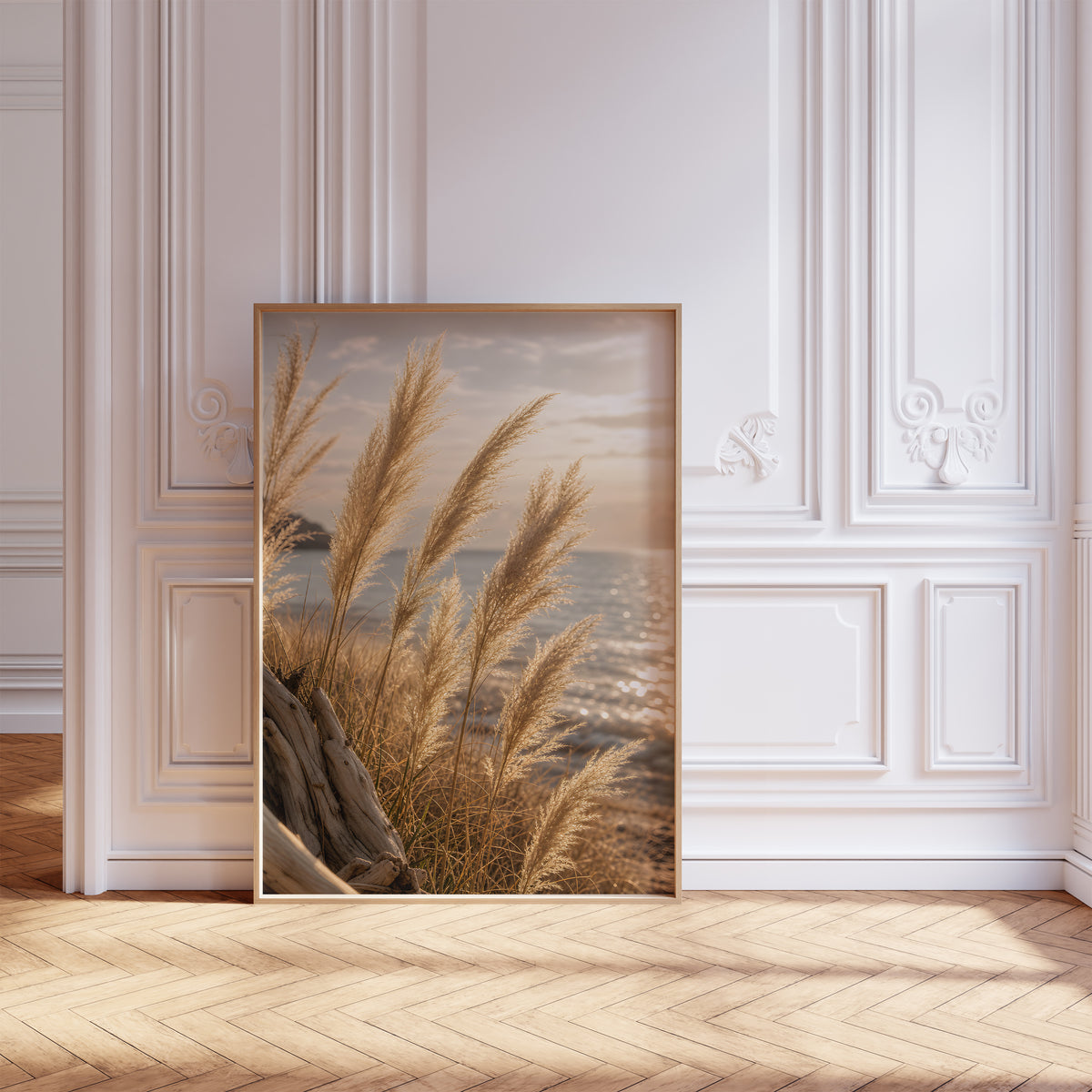 Gerahmtes Poster mit goldenen Pampasgräsern vor glitzerndem Meer im Abendlicht, vor einer weißen Wand mit Zierleisten.