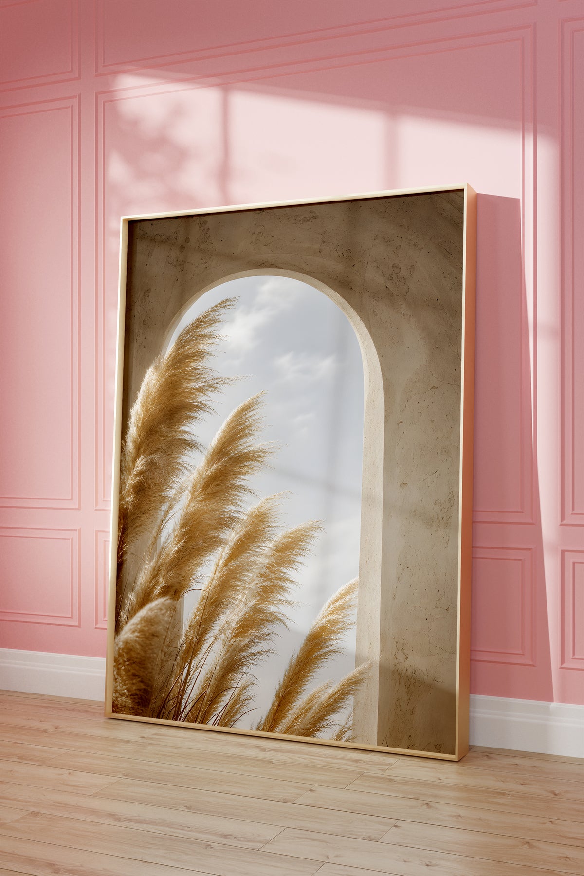 Motiv mit goldenen Pampaswedeln vor einem sandfarbenen Rundbogen mit Blick zum Himmel, als gerahmtes Poster vor einer rosafarbenen Wand.