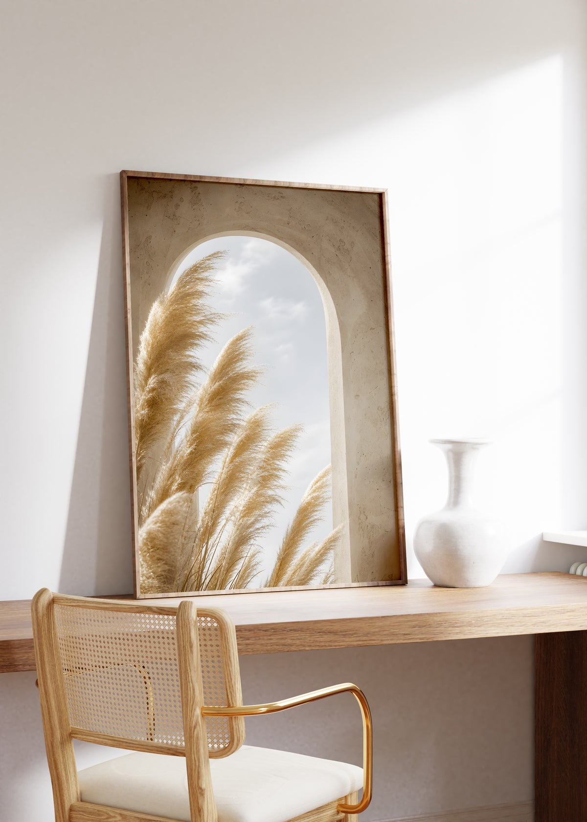 Gerahmtes Poster mit goldenen Pampaswedeln vor einem sandfarbenen Rundbogen mit Blick zum Himmel, auf einem Holztisch neben einer weißen Vase.
