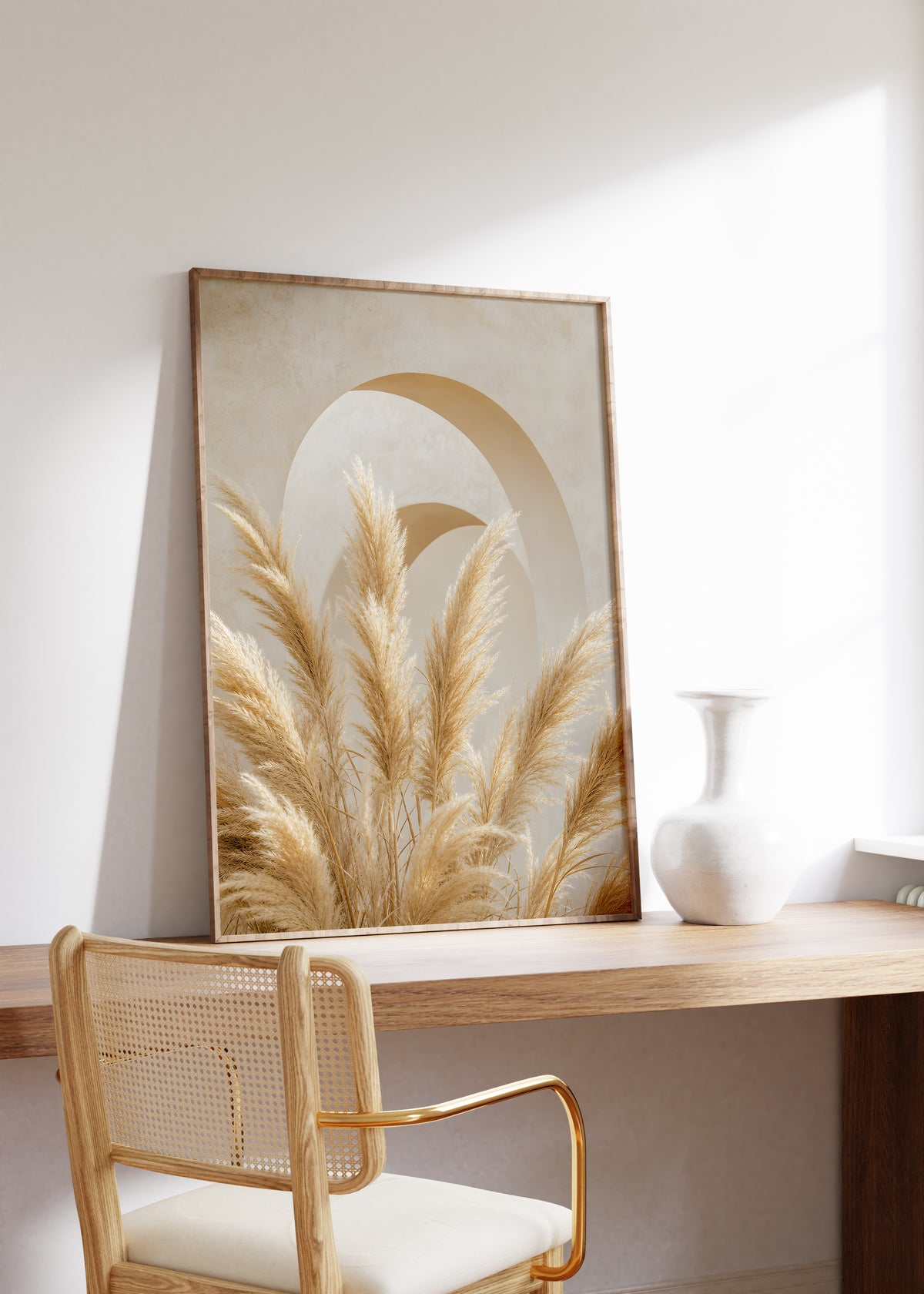 Gerahmtes Poster mit goldbeigen Pampaswedeln vor abstrakten weißen und ockerfarbenen Bögen, auf einem Holztisch neben einer weißen Vase.